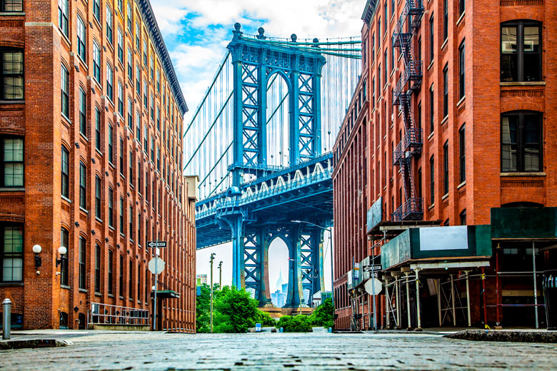 Manhattan Bridge between Manhattan and Brooklyn over East River seen from a narrow alley enclosed by two brick buildings on a sunny day in Washington street in Dumbo, Brooklyn, NYC