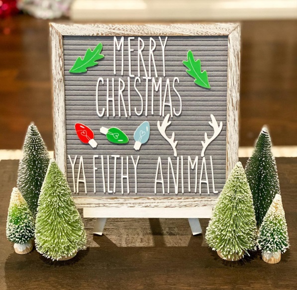 Small sign surrounded by bottle brush trees that says "Merry Christmas ya filthy animal"