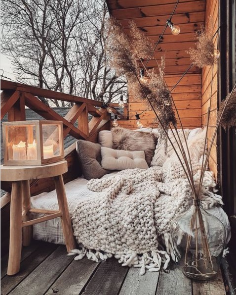 Small balcony decorated for winter with an air mattress, cozy blankets, and pillows
