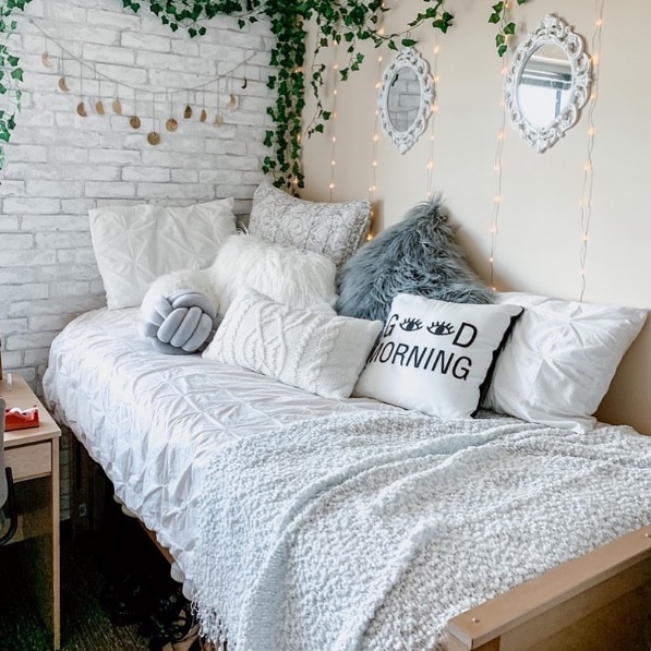 Eclectically decorated corner of a dorm room with a cozy looking bed piled with pillows and blankets