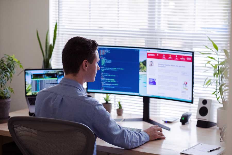 Man sitting at desk and looking at a double computer monitor