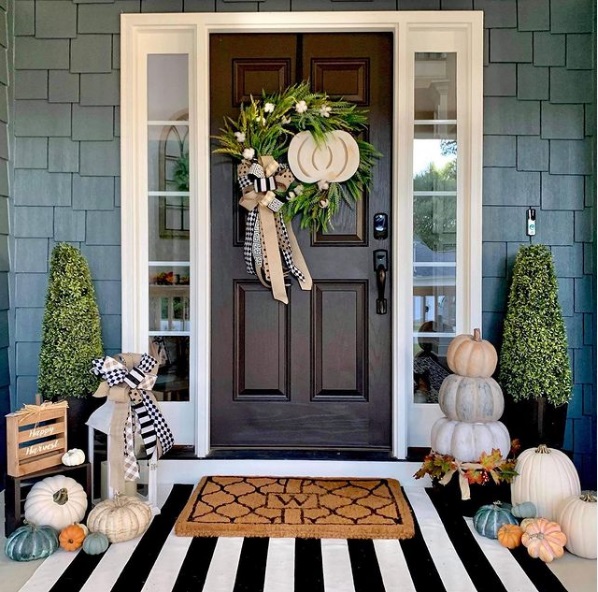 Front porch decorated for fall with pupkins, a doormat, and a wreath