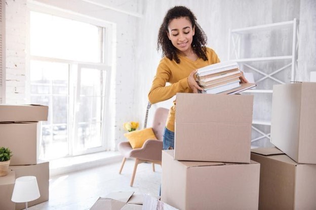 a young woman is packing books into a cardboard moving box