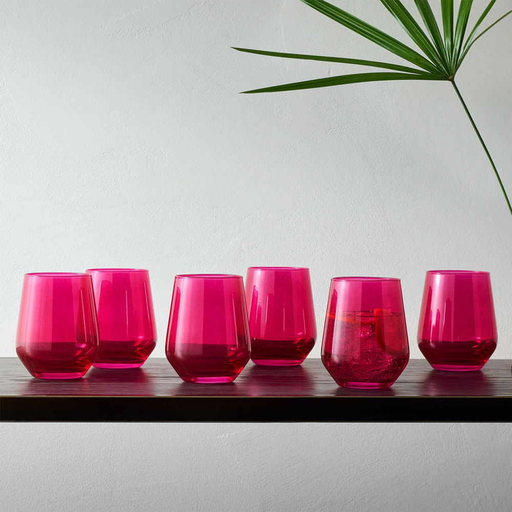 Six short magenta drink glasses lined up on a counter.
