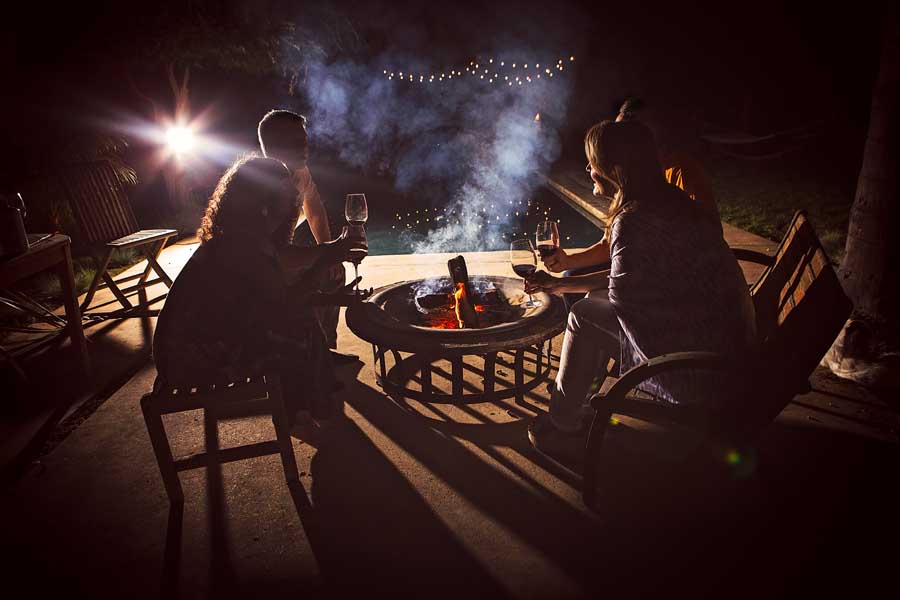 Group of friends sitting around a firepit drinking wine together