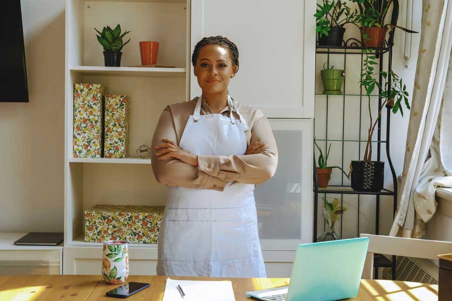 Manager standing with arms crossed in front of laptop and list of their business inventory