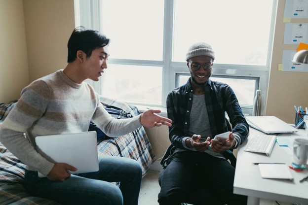 two college students are in a dorm room discussing a project while looking at a phone